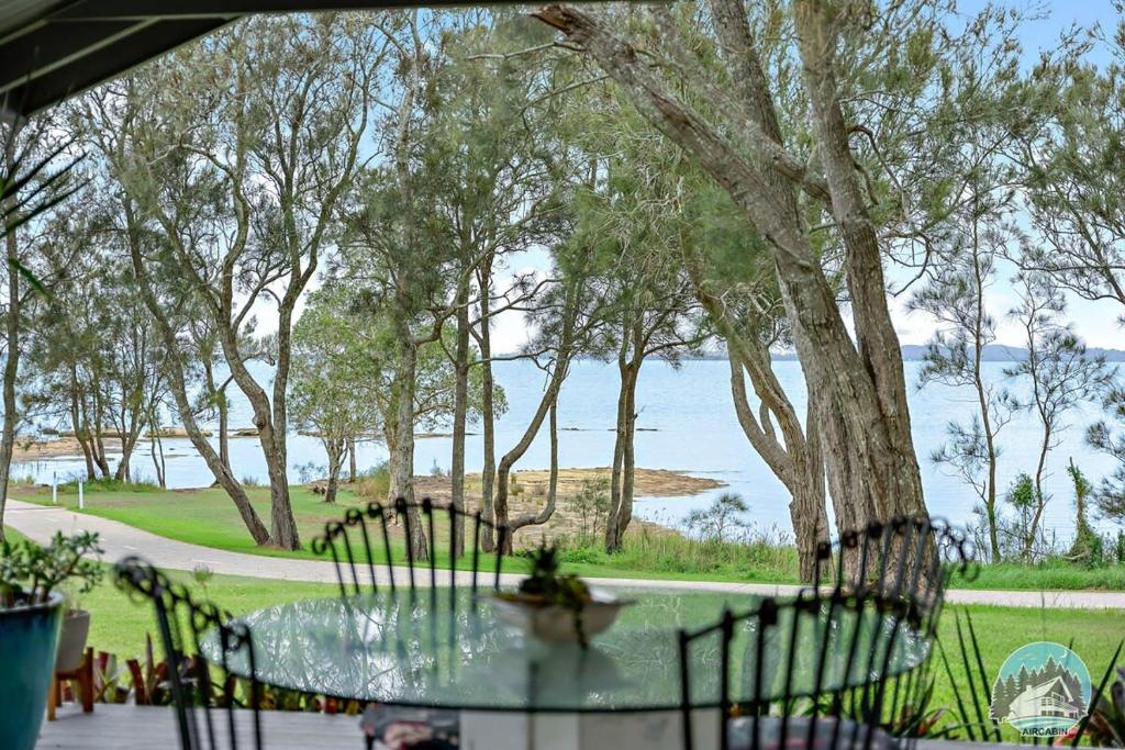 una mesa de cristal y sillas con vistas al agua en Aircabin - Tuggerawong - Waterfront - 4 Beds House, en Karraganbah