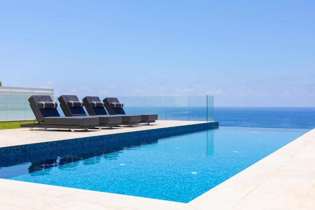 a pool with chairs and the ocean in the background at Cap St Georges Villas in Peyia
