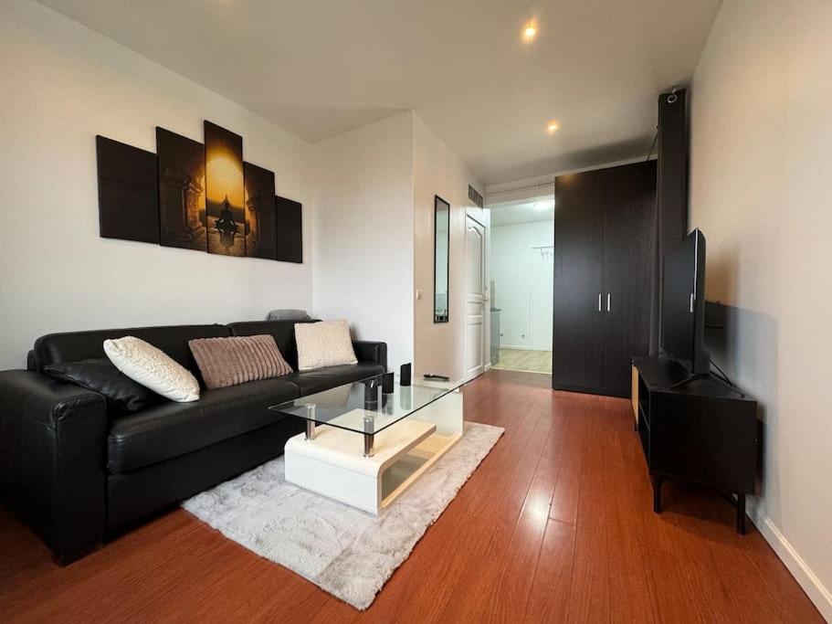 - un salon avec un canapé noir et une table en verre dans l'établissement Logement calme et cosy au Centre-Ville, à Saint-Cyr-lʼÉcole
