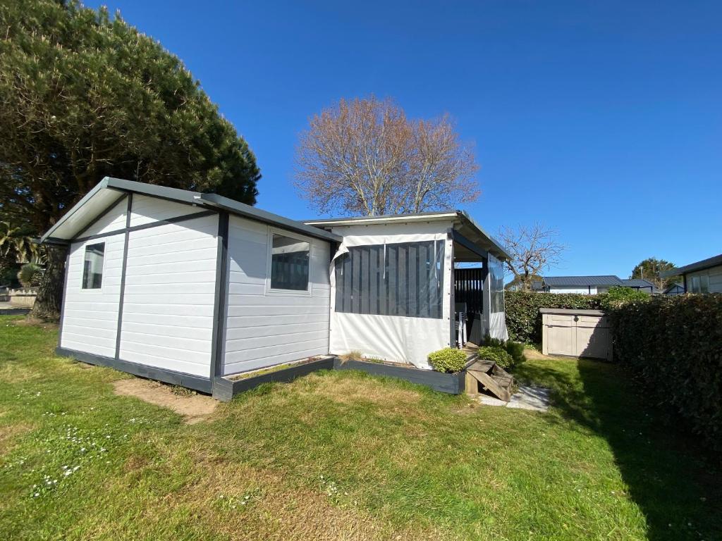 un petit hangar blanc dans une cour herbeuse dans l'établissement Chalet situé dans un camping 4 étoiles - 4 à 6 personnes - KIRIO, à Guidel