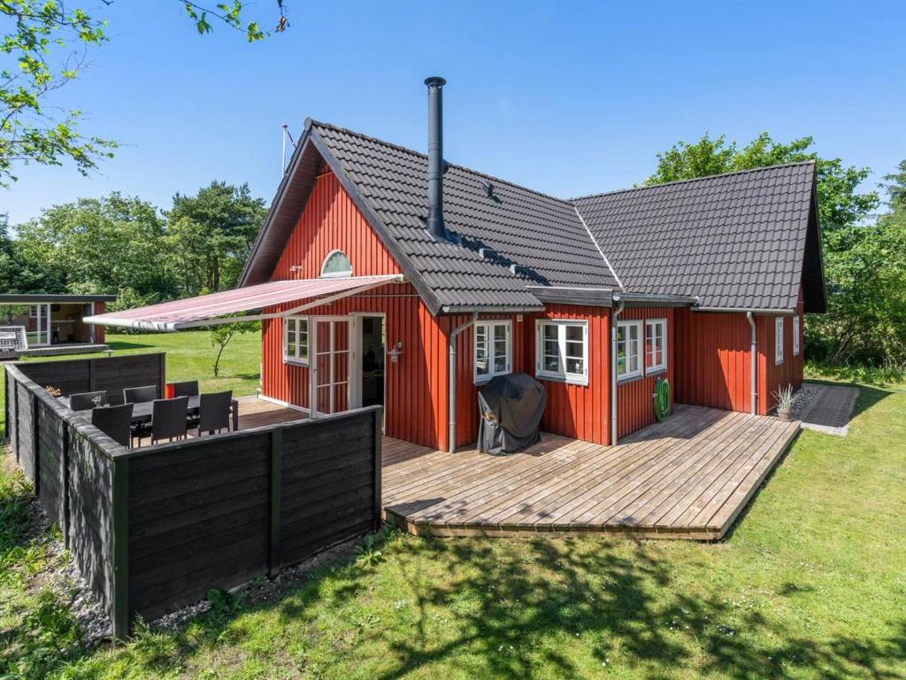 uma casa vermelha com um deque de madeira no quintal em Holiday Home Soile - all inclusive - 12km from the sea by Interhome em Oksbøl