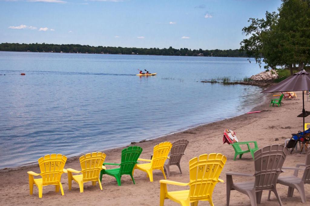 a group of chairs on a beach with a boat in the water at Newly Renovated 3 Bedroom Beach Front Condo 1B in Lanark