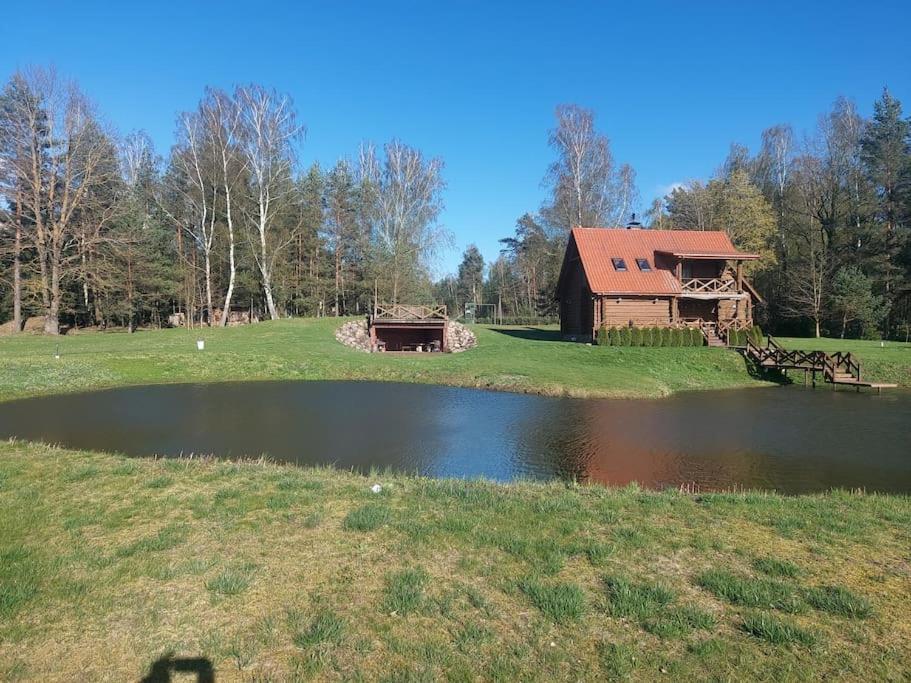 a barn and a pond in a field with a house at Poilsio namelis in Kaišiadorys