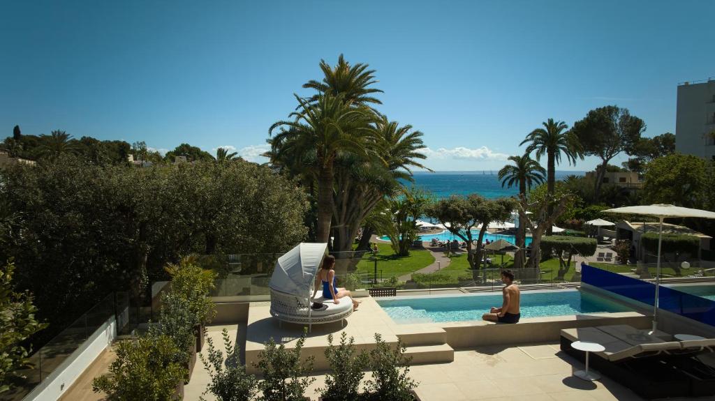 two people sitting by a swimming pool at a resort at Hotel Son Caliu Spa Oasis in Palmanova