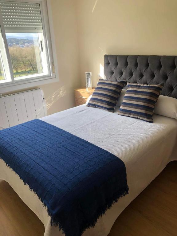 a blue and white bed with blue pillows and a window at Casa Aricel VT in Chantada