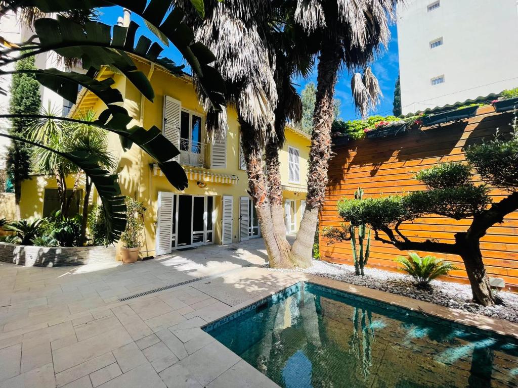 basen przed żółtym budynkiem z palmami w obiekcie L'Eden House - Maison hyper centre plages 2min à pied piscine w mieście Antibes
