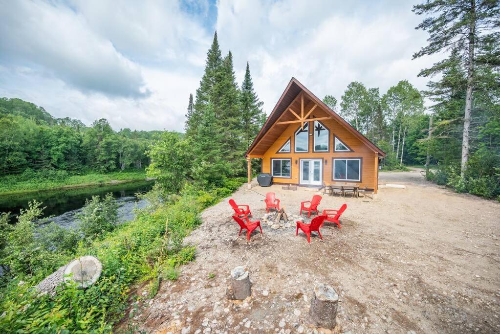 a small cabin with red chairs in front of it at Riverside Retreat: Maazah Cottage in Fort Coulonge