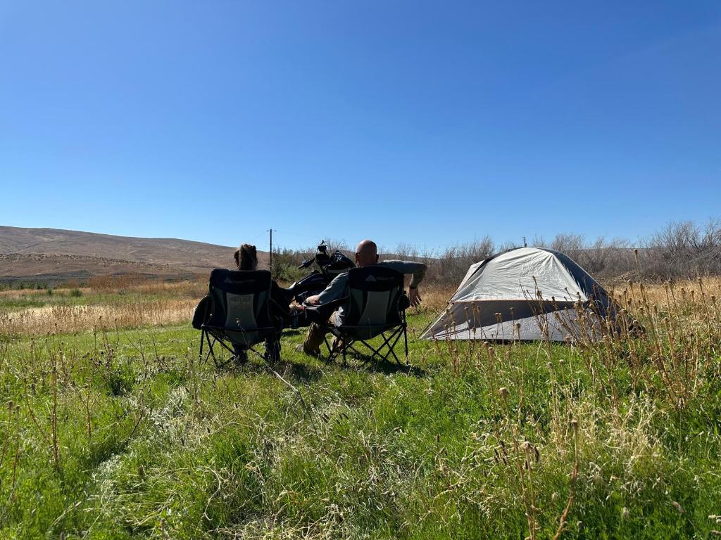 Infidel Acres Motorcycle Campground في Naches: مجموعة من ثلاثة أشخاص يجلسون في كراسي بجوار خيمة