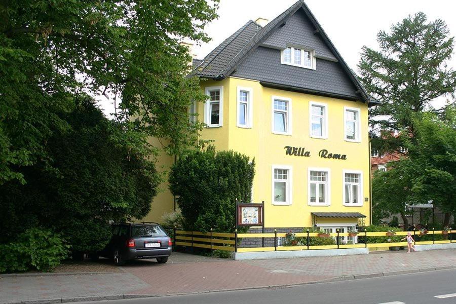 un bâtiment jaune avec un toit noir dans une rue dans l'établissement Willa Roma, à Świnoujście