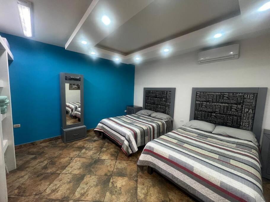 twee bedden in een kamer met blauwe muren en een spiegel bij GR20acd Elva in Cuauhtémoc