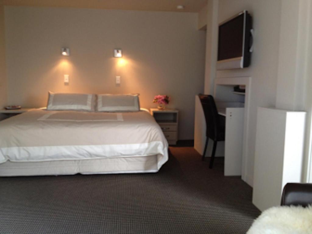 een slaapkamer met een bed, een bureau en een televisie bij Heriot Lane City Apartments in Dunedin