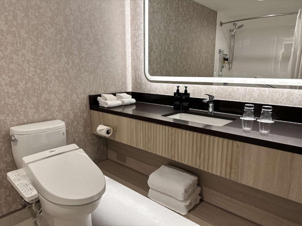 La salle de bains est pourvue de toilettes, d'un lavabo et d'un miroir. dans l'établissement Coast Victoria Hotel & Marina by APA, à Victoria