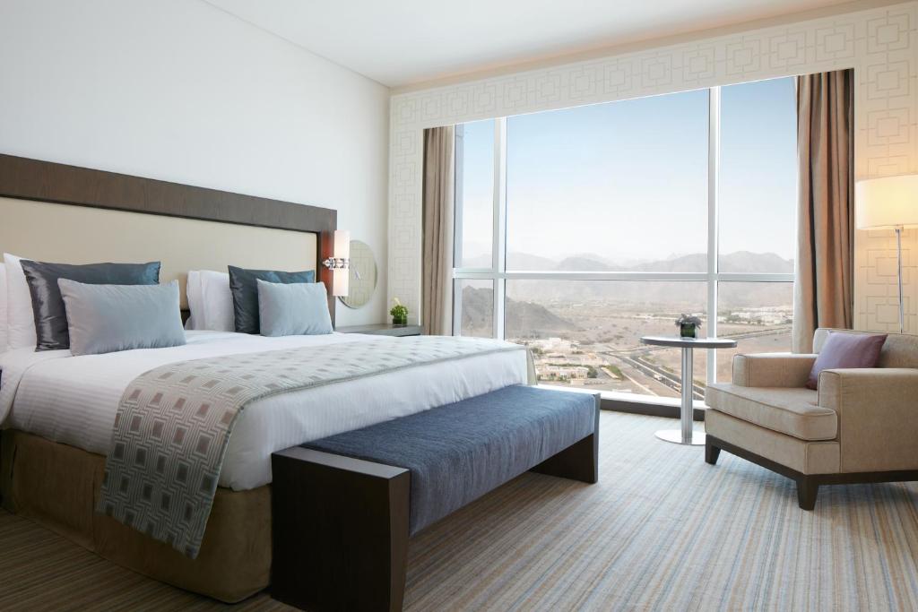 a bedroom with a bed and a chair and a large window at Royal M Hotel Fujairah by Gewan in Fujairah