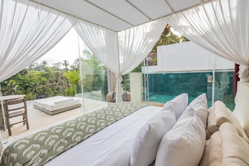 a bedroom with a large white bed and glass walls at Villa Cella Bella Ubud in Ubud