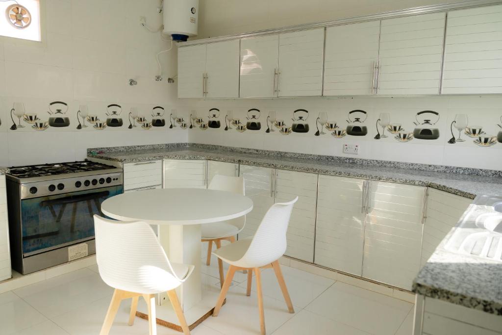 a white kitchen with a white table and chairs at Al Fay Farmhouse in Sinādil