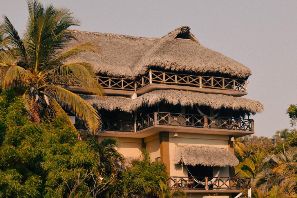 een gebouw met een rieten dak en een palmboom bij Beach Front Guesthouse in Puerto Escondido