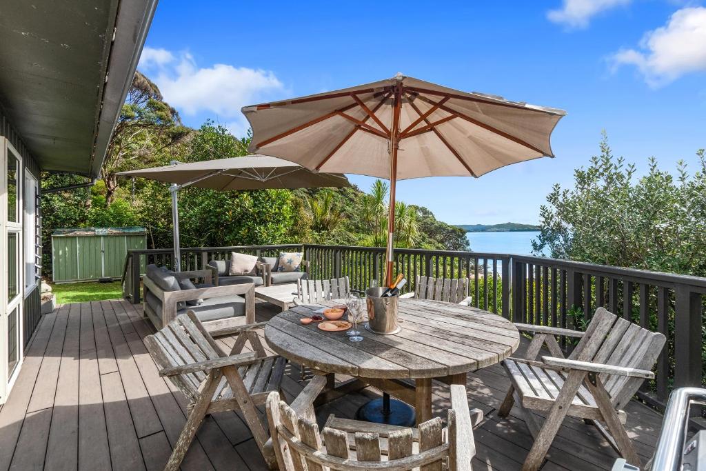 Kereru Cottage - Matapouri Holiday Home في وانغاري: طاولة وكراسي خشبية مع مظلة على سطح السفينة