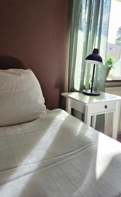 アーベスタにあるLilla Älvbrogården i stanのベッドルーム(白いベッド1台、テーブルの上にランプ付)