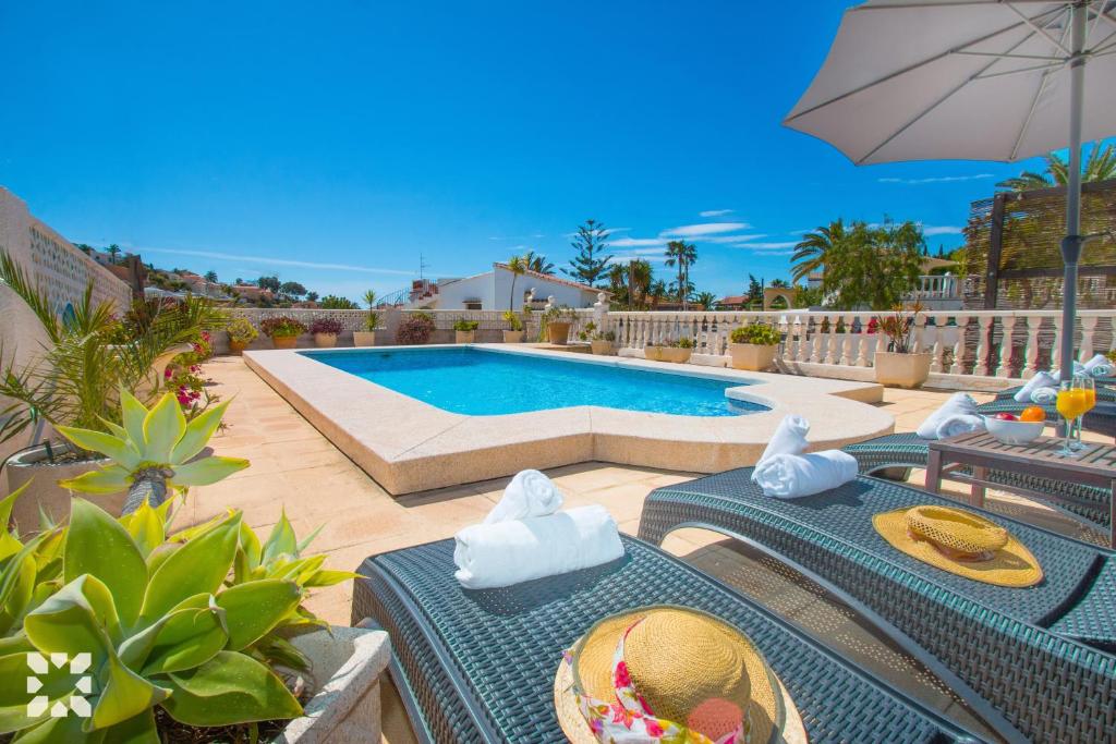 una piscina con mesas, sillas y una sombrilla en Villa Puerto Blanco by Abahana Villas, en La Canuta