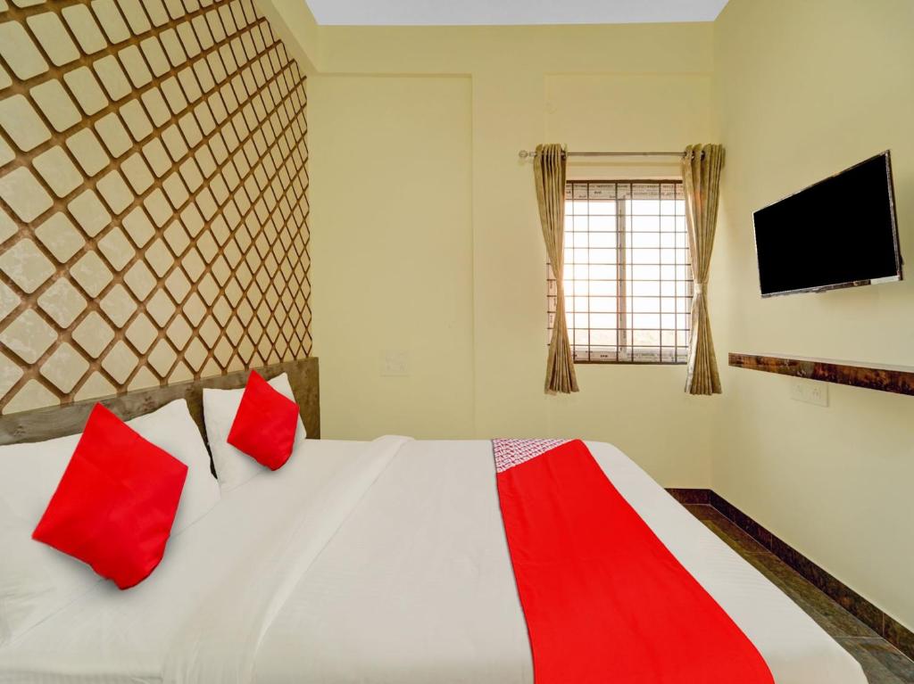 a bedroom with a bed with red pillows and a television at OYO Flagship Mathrushree Lodge in Yelahanka