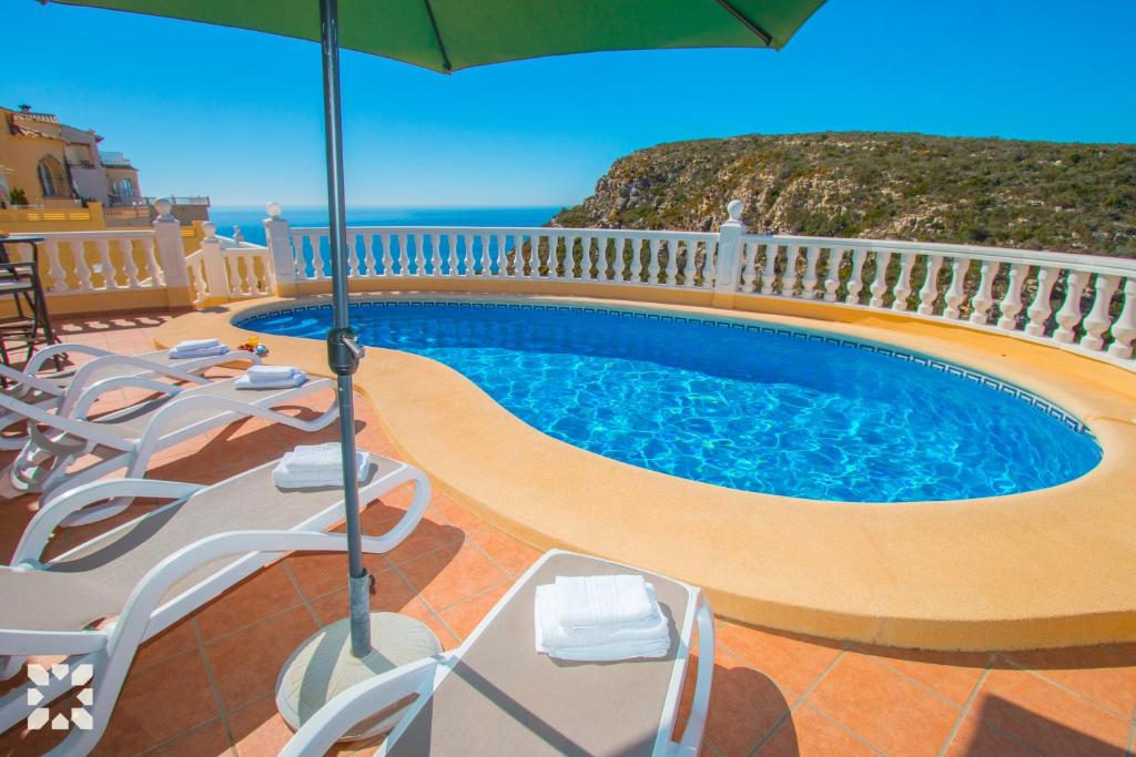 a swimming pool with chairs and an umbrella at Villa Octavio by Abahana Villas in Benitachell