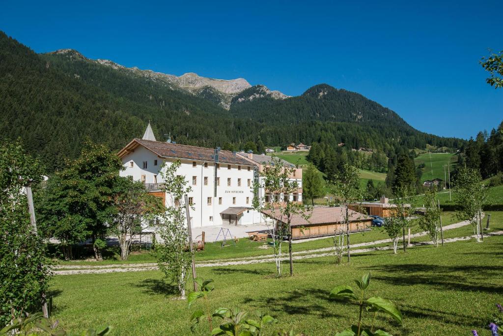 a building in a field with mountains in the background at Zum Hirschen Boutique Hotel Nonsberg in Unsere Liebe Frau im Walde