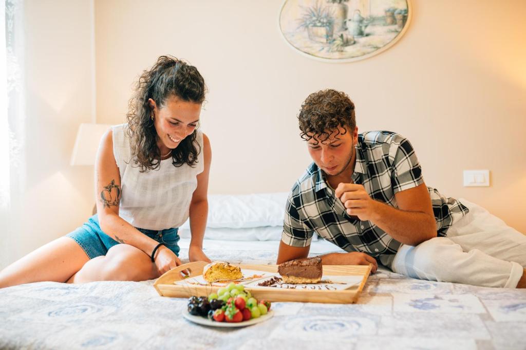 a man and woman sitting on a bed with a plate of food at Hotel Ponte Molo in Porto Tolle