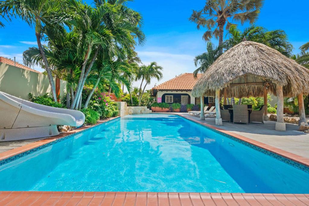 a swimming pool with a resort style house with palm trees at Pool VillaJacuzziFREE Utilities3minPalm Beach in Noord