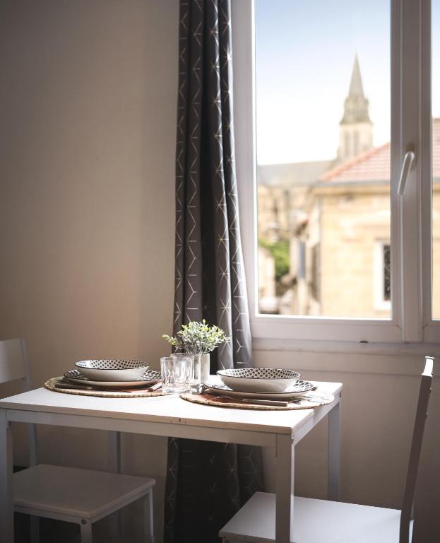 une table avec des assiettes, des verres et une fenêtre dans l'établissement Le petit chez vous - T1 Bergerac -2 pers, à Bergerac