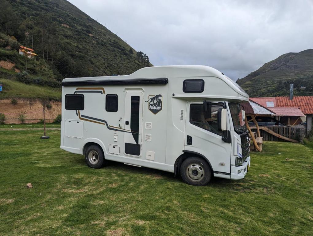 Casa Rodante amplia en Cusco في كوسكو: قافلة بيضاء متوقفة في حقل مع جبل
