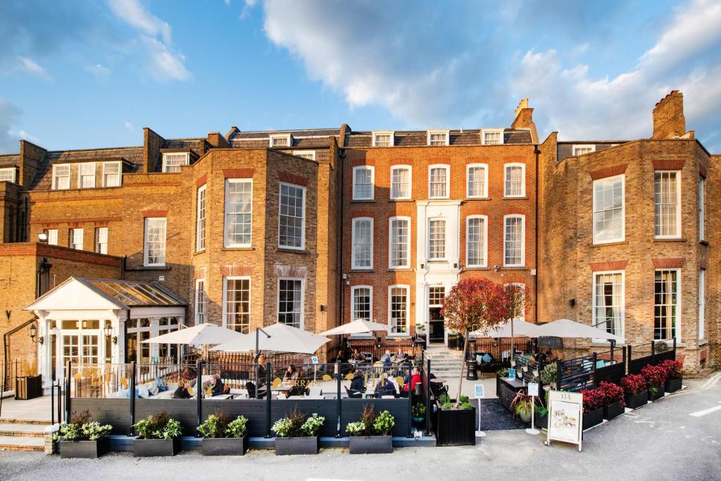ein großes Backsteingebäude mit Tischen und Sonnenschirmen davor in der Unterkunft Richmond Hill Hotel in Richmond upon Thames