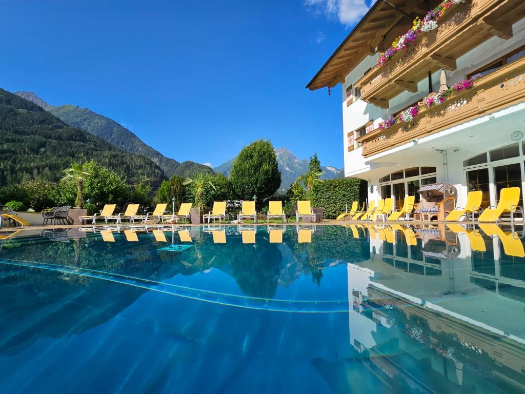 uma piscina de hotel com cadeiras e montanhas ao fundo em Hotel Edenlehen em Mayrhofen