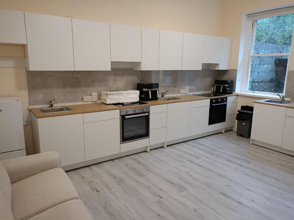 uma cozinha com armários brancos, um lavatório e um sofá em Dublin Palm 2 em Dublin