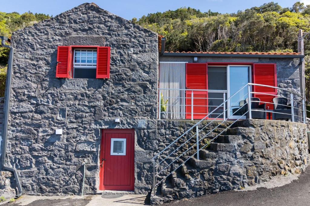 uma casa de pedra com persianas vermelhas e uma porta vermelha em Cantinho dos Cagarros em Lajes do Pico