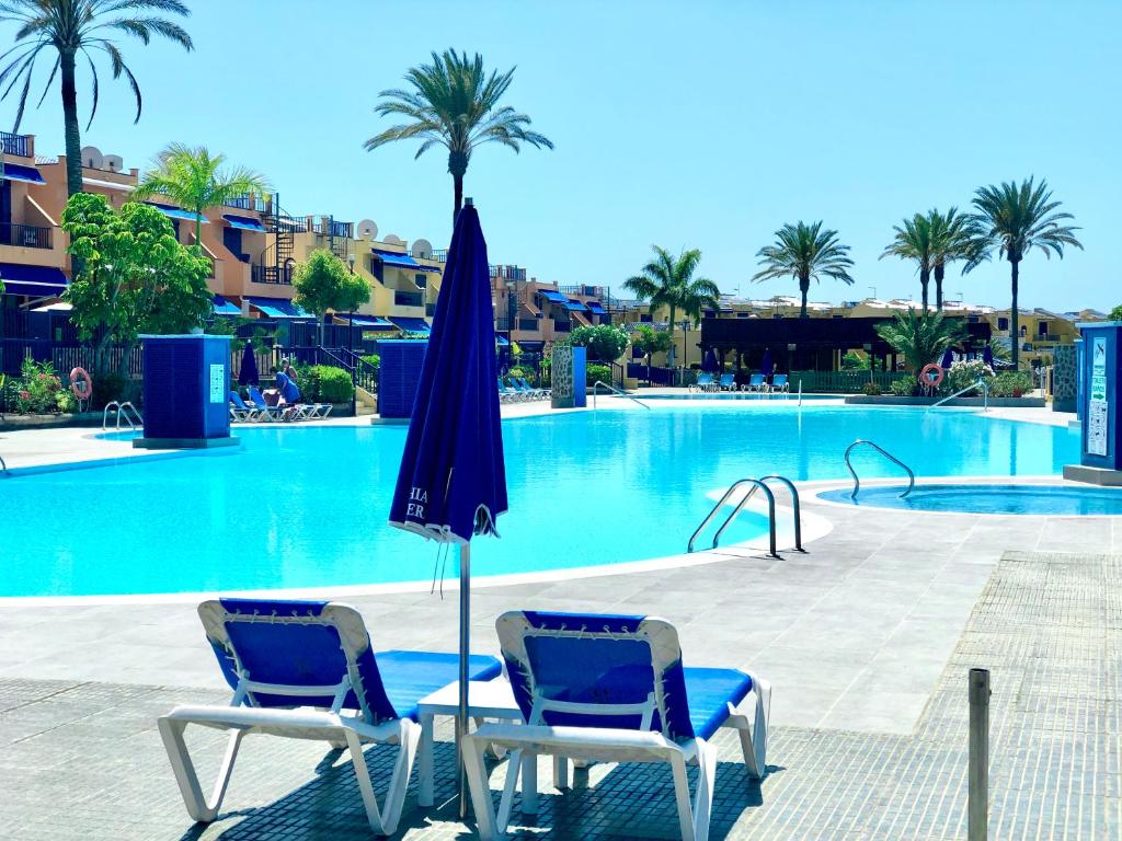 duas cadeiras e um guarda-sol em frente a uma piscina em Beach and golf 4 Bedroom Holiday Home em Maspalomas