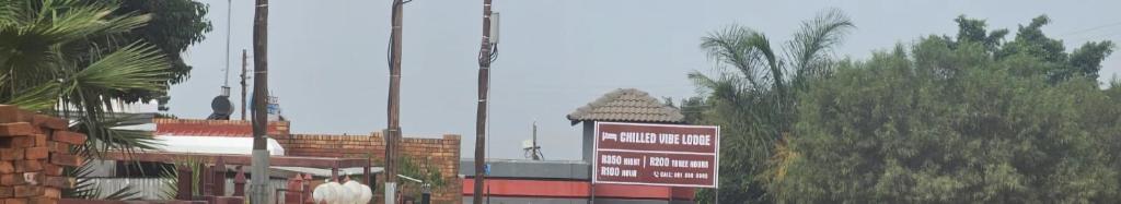 a sign in front of a building with trees at Chilled Vibe Lodge in Soshanguve
