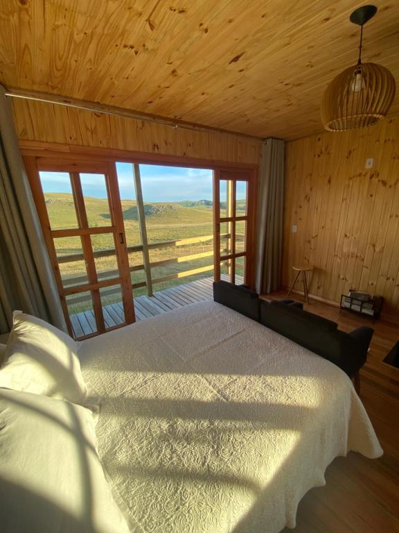 um quarto com uma cama e uma grande janela em Chalé Campos Da Serra em São José dos Ausentes