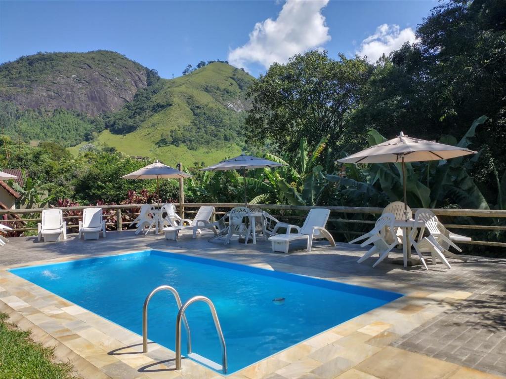 una piscina con sillas y sombrillas con montañas en el fondo en Pousada dos Anjos, en São Pedro da Serra
