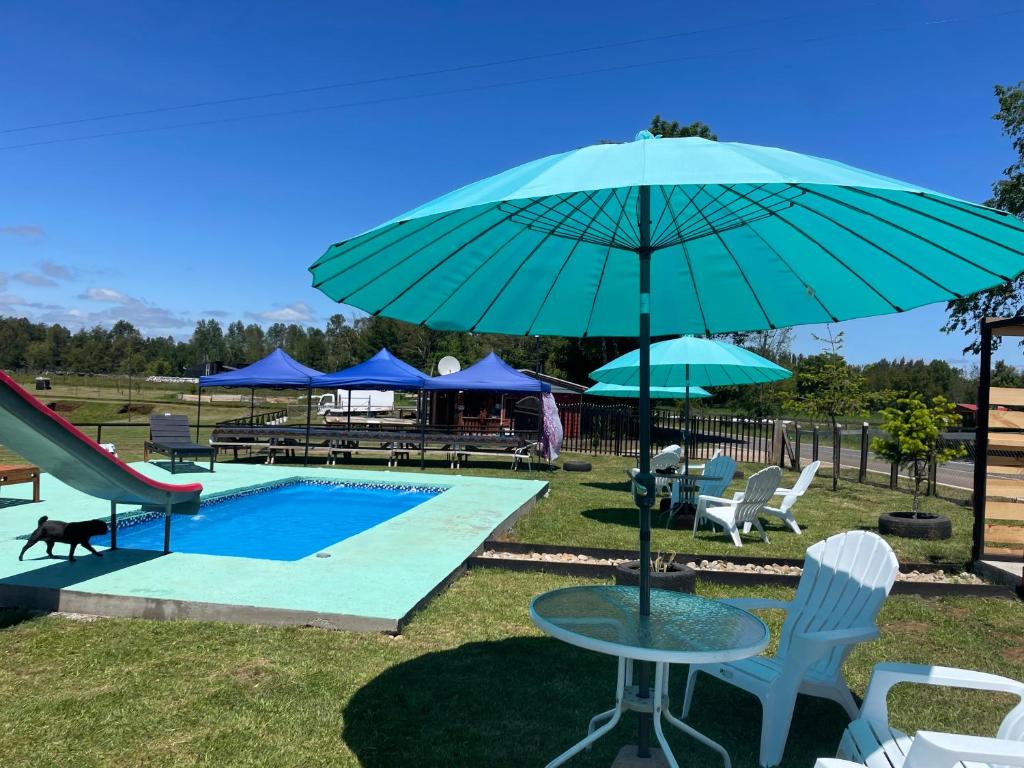 a pool with a table and a blue umbrella at El pantano de sherk y fiona in San José de la Mariquina