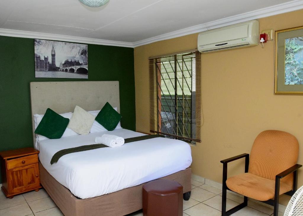a bedroom with a bed and a chair in it at Obasi Green Inn Guesthouse in Roodepoort