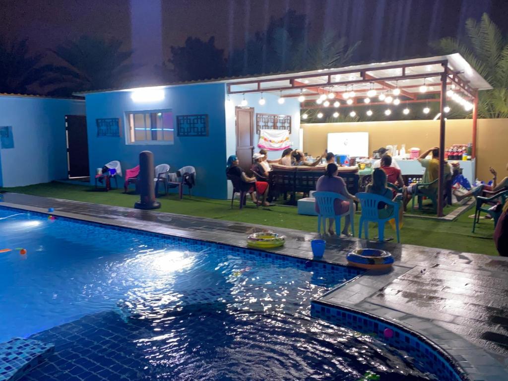 een groep mensen die 's nachts rond een zwembad zitten bij Al Rahba Holiday Farmhouse in Al Rahba