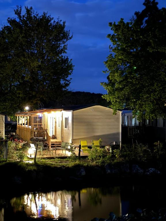 Una caravana iluminada por la noche junto a un estanque en Mobil home tout confort Camping Les VIVIERS CAP FERRET en Lège-Cap-Ferret