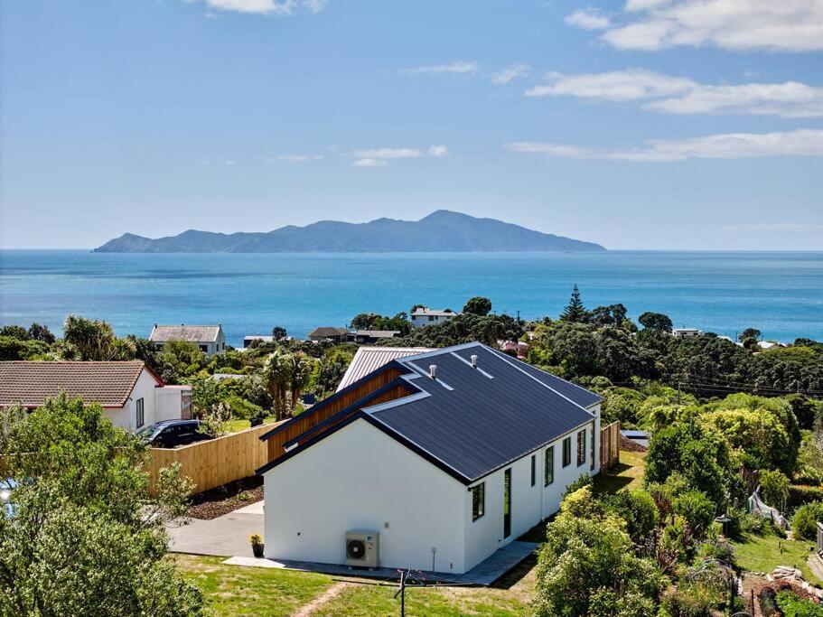 a white house with a solar roof next to the ocean at Tranquility on the Hill Outdoor Bath 30 mins to city by train or car in Wellington