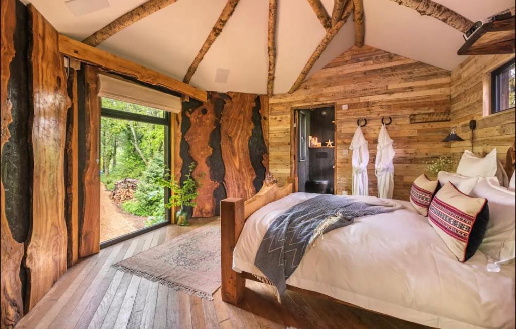 a log cabin bedroom with a bed and a large window at Unique Secluded Romantic Treehouse in Cornwall, sleeps 2 in Looe