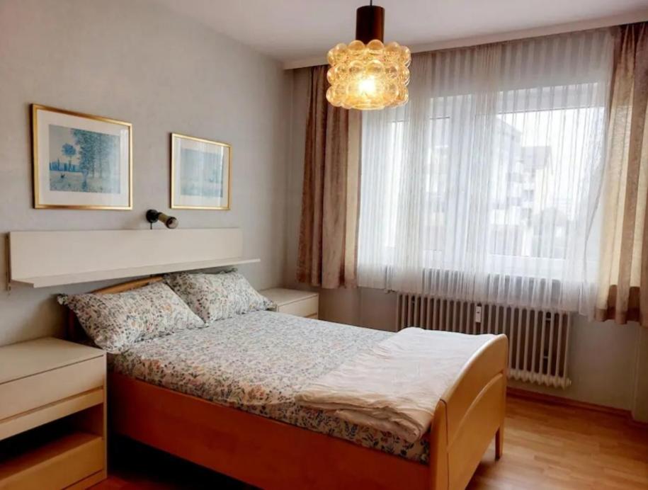 een slaapkamer met een bed, een kroonluchter en een raam bij 1Room in a beautiful shared apartment 12min walk from Center in Friedrichshafen