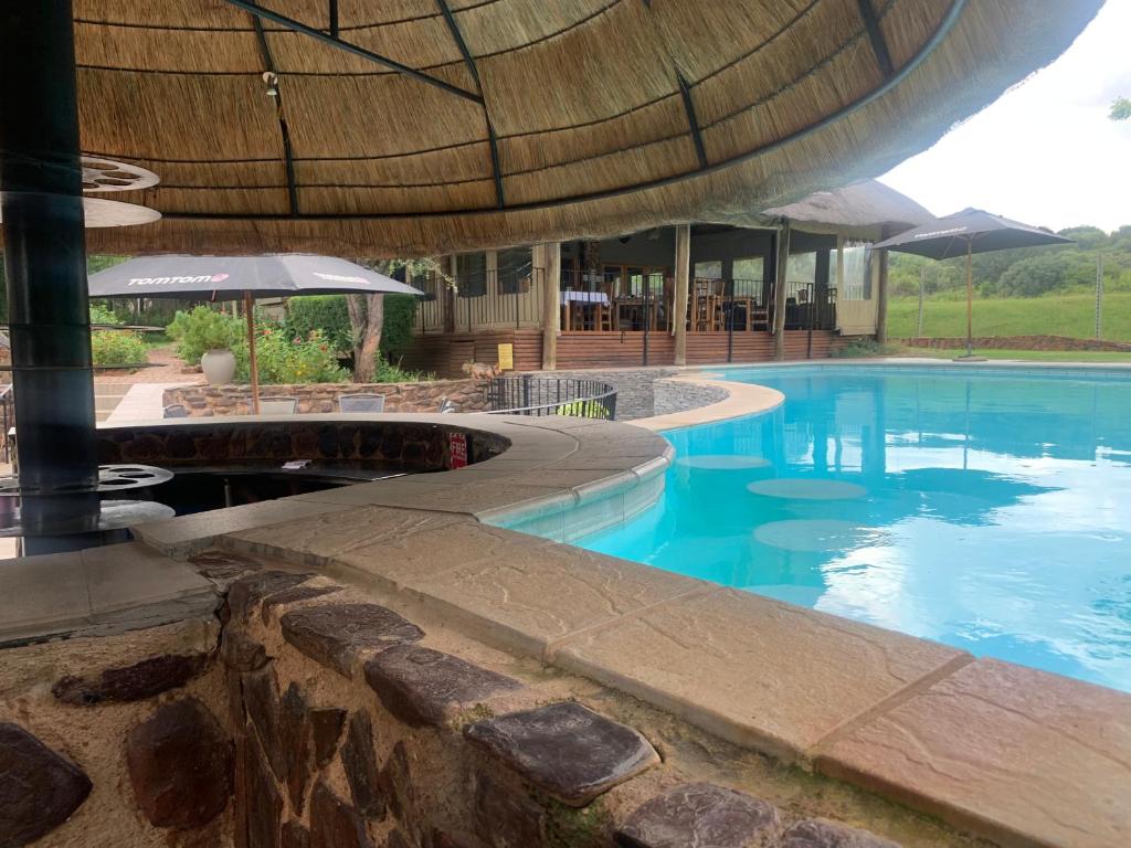 a large swimming pool with a building with a roof at Tidimalo Lodge in Rustenburg
