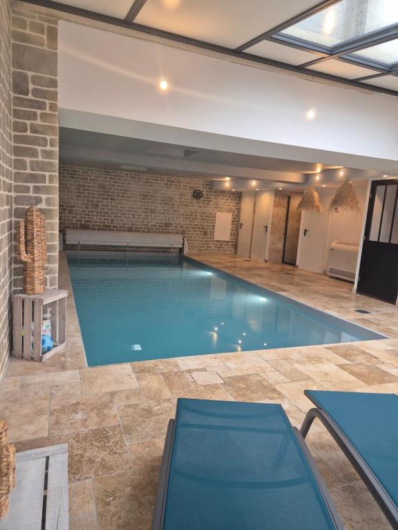 einen großen Pool in einem Zimmer mit Ziegelwand in der Unterkunft Villa avec piscine intérieure proche des plages du debarquement in Escoville
