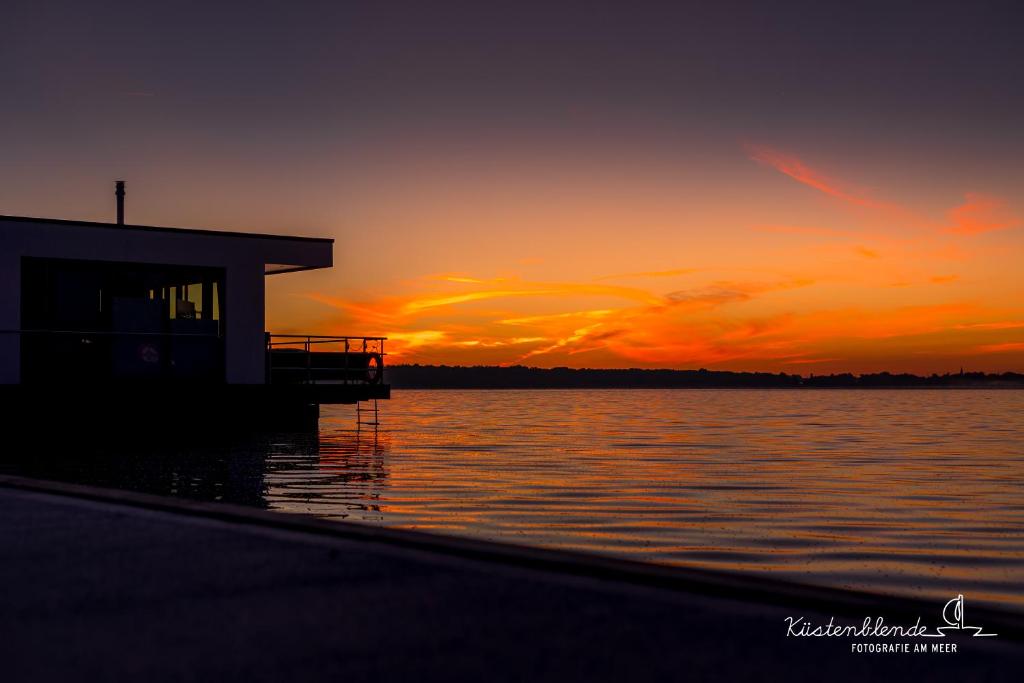 una puesta de sol sobre un cuerpo de agua con un edificio en Hausboot Arielle, en Ribnitz-Damgarten