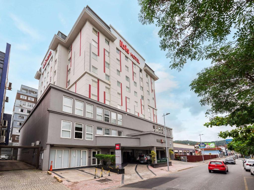 a large white building with a red sign on it at ibis Joinville in Joinville