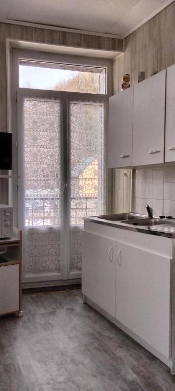 une cuisine avec des placards blancs et une grande fenêtre dans l'établissement Résidence les Sources Mont Dore, à Mont-Dore